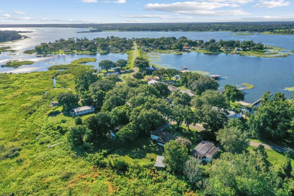 An aerial view shows houses nestled among trees on a peninsula surrounded by a lake — 10865 SE TIMUCUAN ROAD, SUMMERFIELD, FL