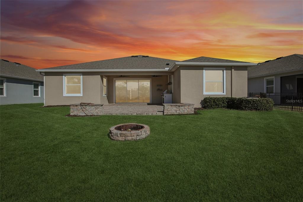 The backyard features a stone fire pit, a paved patio, and a tan stucco house exterior — 10747 LAXER CAY LOOP, SAN ANTONIO, FL
