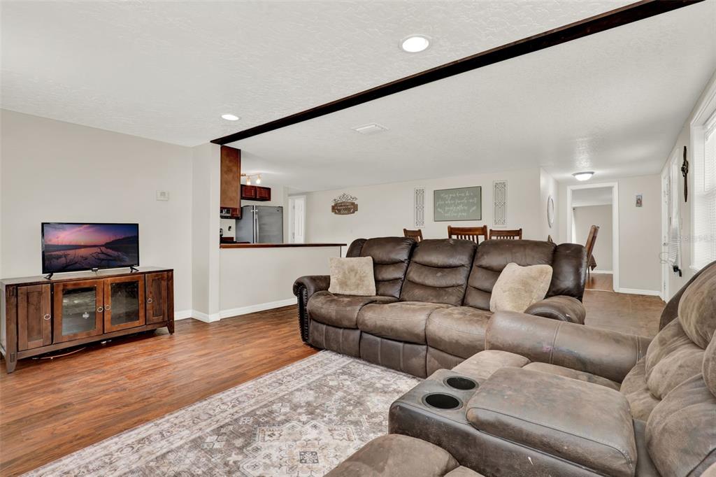 A living room with wood-look flooring, a brown leather sofa, and an open kitchen view — 30137 ORANGE AVENUE, SORRENTO, FL