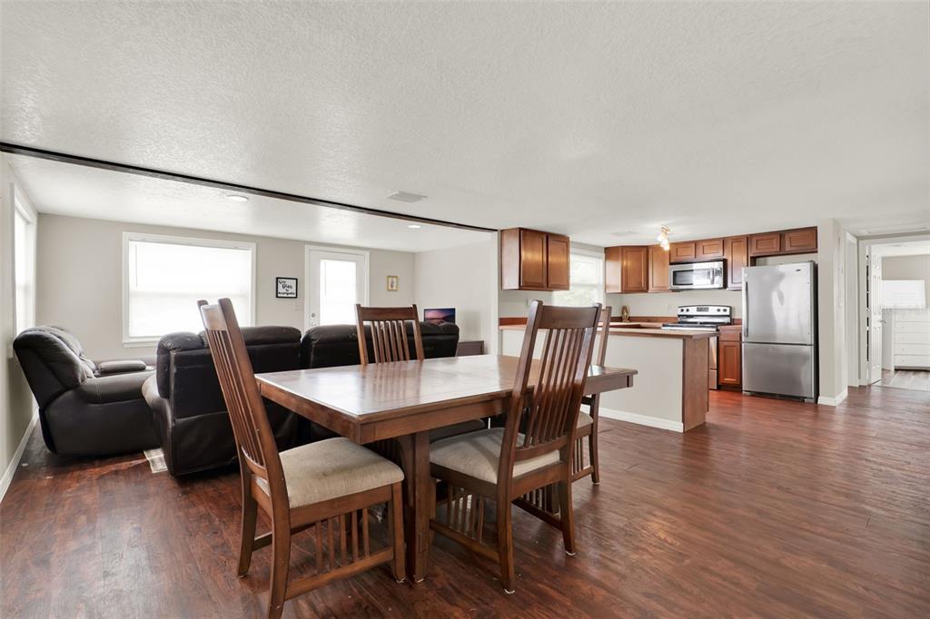 An open-concept living and dining area features wood-look flooring, a wooden dining set, and kitchen — 30137 ORANGE AVENUE, SORRENTO, FL