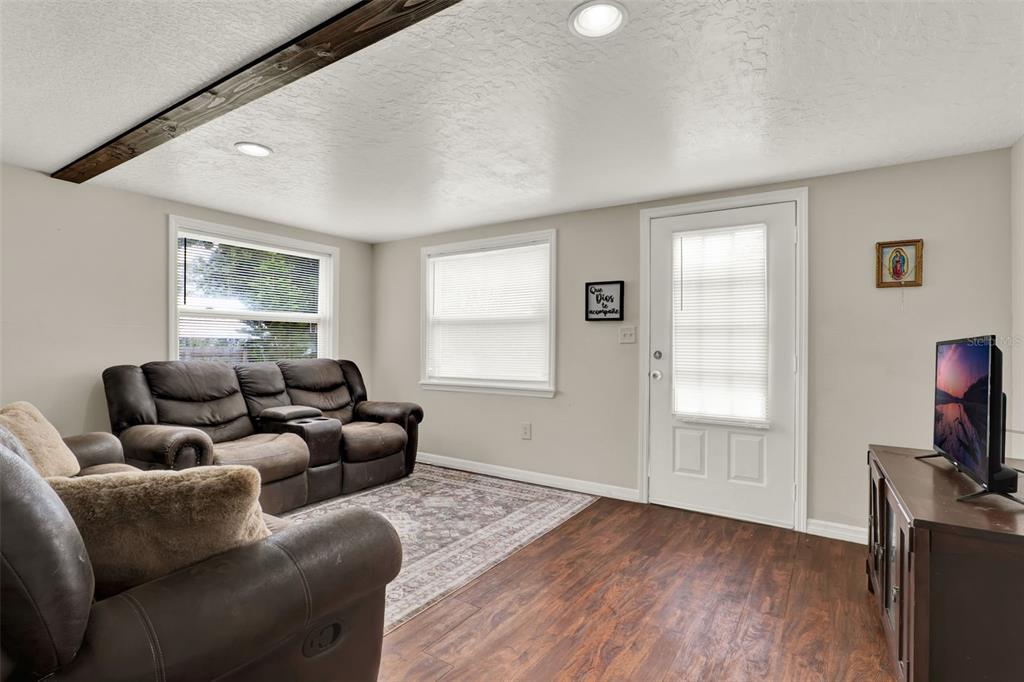 A living room features a brown reclining sofa, wood-look flooring, a ceiling beam, and a television — 30137 ORANGE AVENUE, SORRENTO, FL