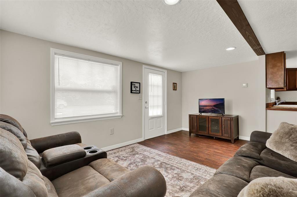 A living room features brown sofas, a television on a wooden stand, and wood flooring — 30137 ORANGE AVENUE, SORRENTO, FL