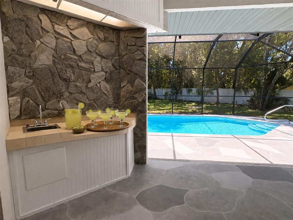 A covered patio features wicker furniture, a stone accent wall, and a swimming pool — 18608 AUTUMN LAKE BOULEVARD, HUDSON, FL