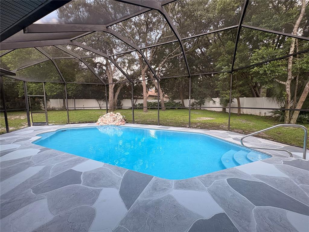 A swimming pool with a stone deck is enclosed by a screened lanai in a backyard — 18608 AUTUMN LAKE BOULEVARD, HUDSON, FL