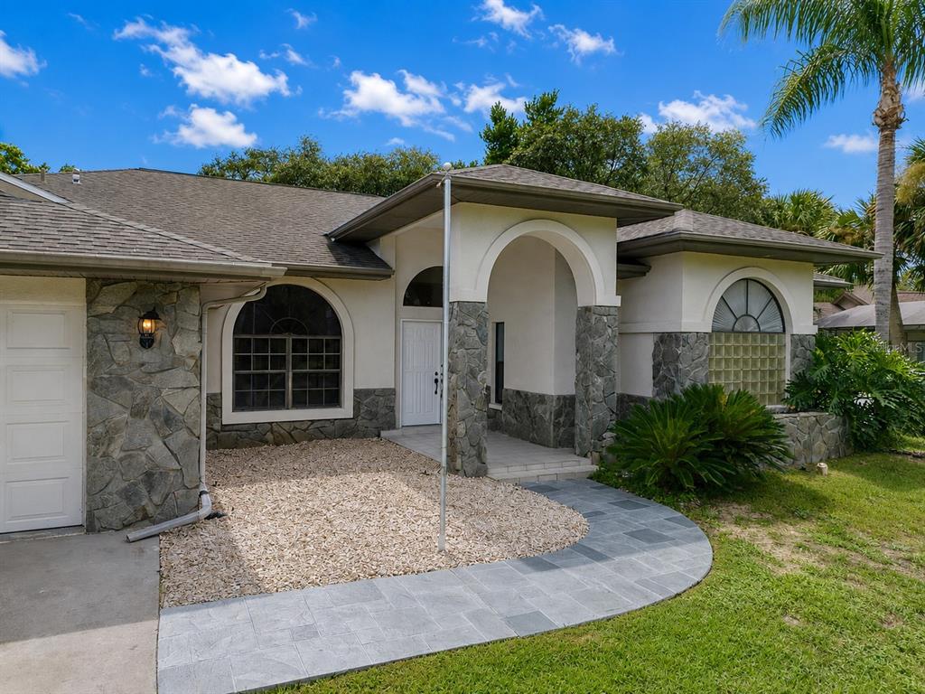 The exterior entrance features a tiled porch, double white doors, and stone-clad support columns — 18608 AUTUMN LAKE BOULEVARD, HUDSON, FL
