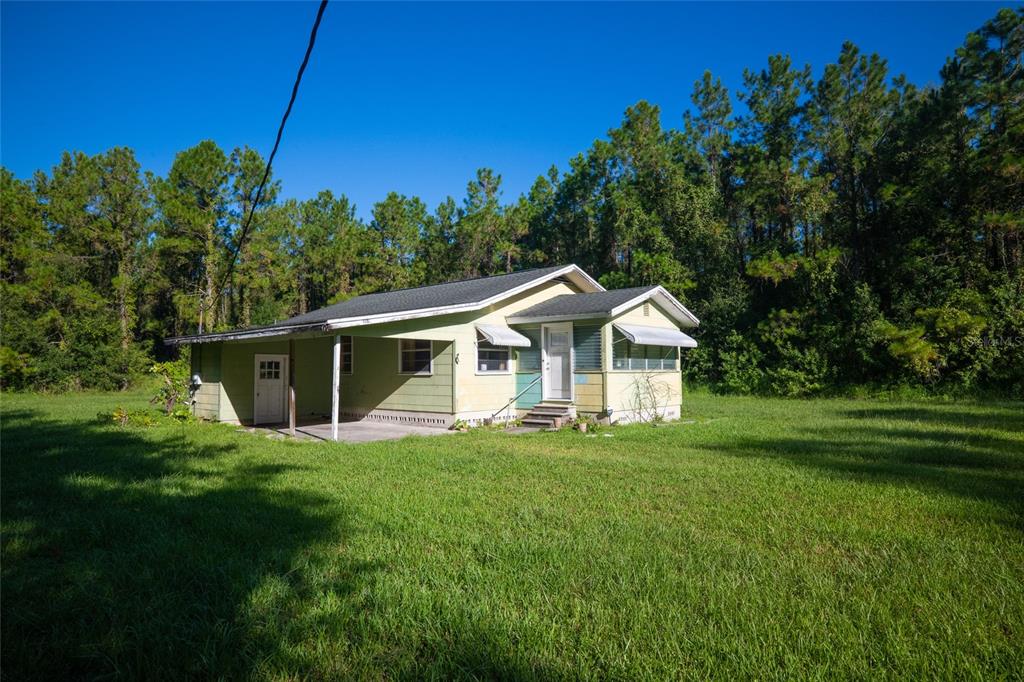 A single-story house with a carport and light green siding sits on a grassy lot — 5151 DREXEL ROAD, LAND O LAKES, FL