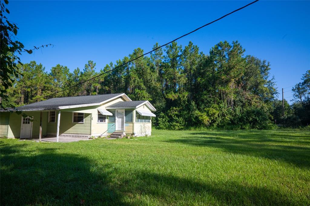 A single-story house with light green siding sits on a large, grassy lot near trees — 5151 DREXEL ROAD, LAND O LAKES, FL