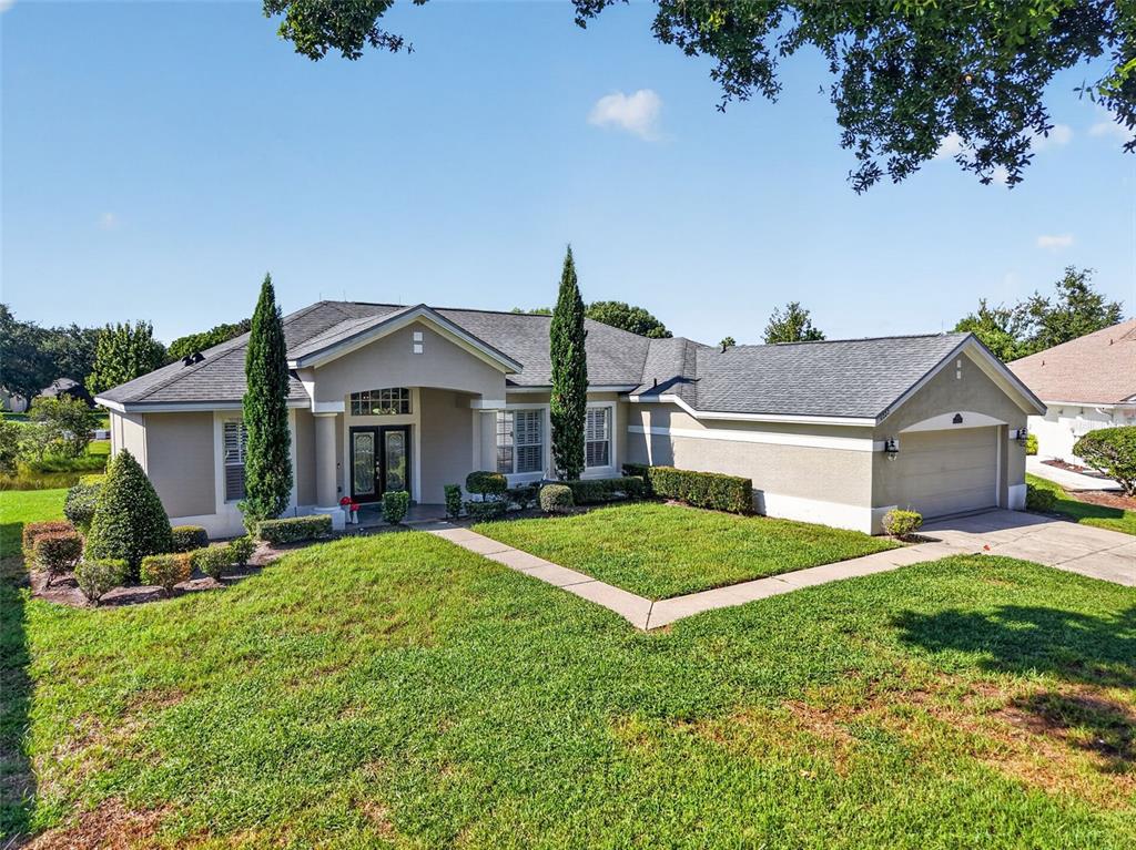 A single-story house with a beige exterior, a gray shingled roof, and a two-car garage — 6022 FALCONBRIDGE PLACE, MOUNT DORA, FL