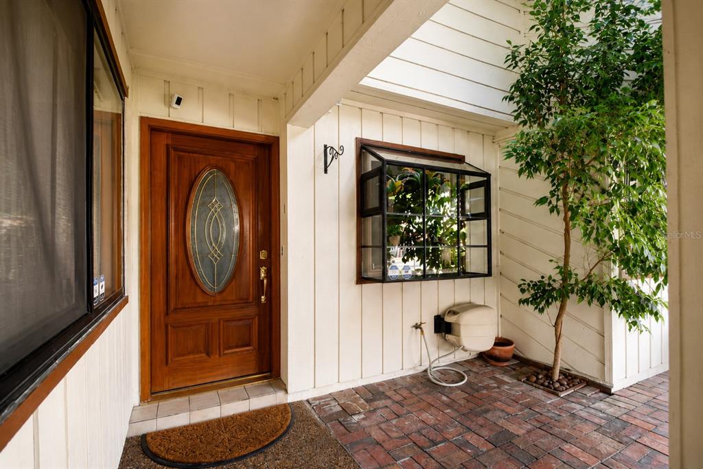 A wooden front door with an oval glass insert sits beside a greenhouse window — 3884 VILLA ROSE LANE, ORLANDO, FL