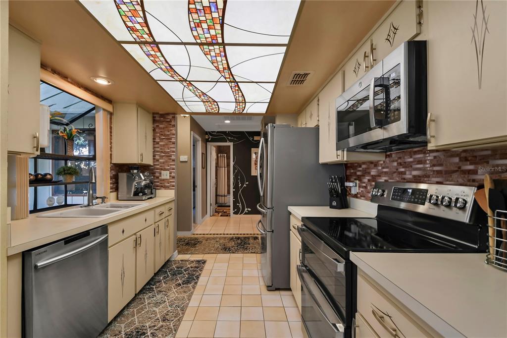 A galley kitchen features cream cabinets, stainless steel appliances, a tiled backsplash, and a decorative ceiling — 3884 VILLA ROSE LANE, ORLANDO, FL