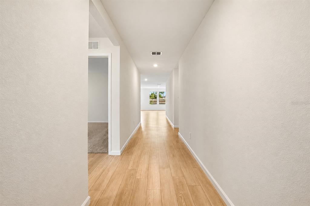 A long hallway with light wood-look flooring leads to a bright room with windows — 3841 AMERS LOOP, HAINES CITY, FL
