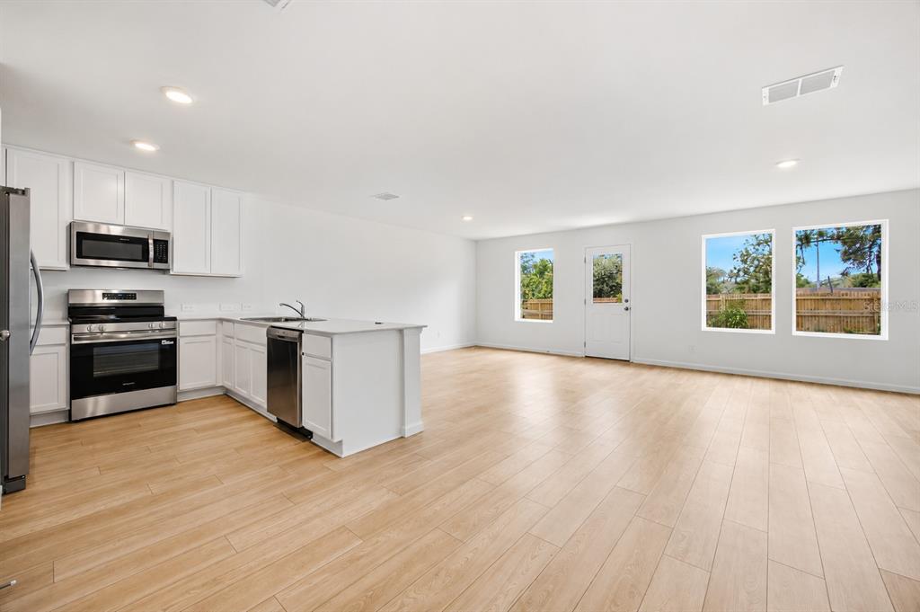 A modern kitchen with white cabinets and stainless steel appliances opens into a spacious living area — 3841 AMERS LOOP, HAINES CITY, FL