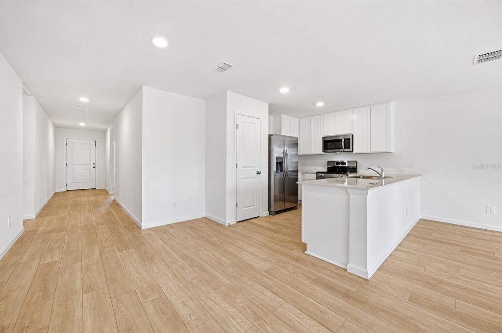 A kitchen with white cabinets, stainless steel appliances, and an island opens to a hallway — 3841 AMERS LOOP, HAINES CITY, FL