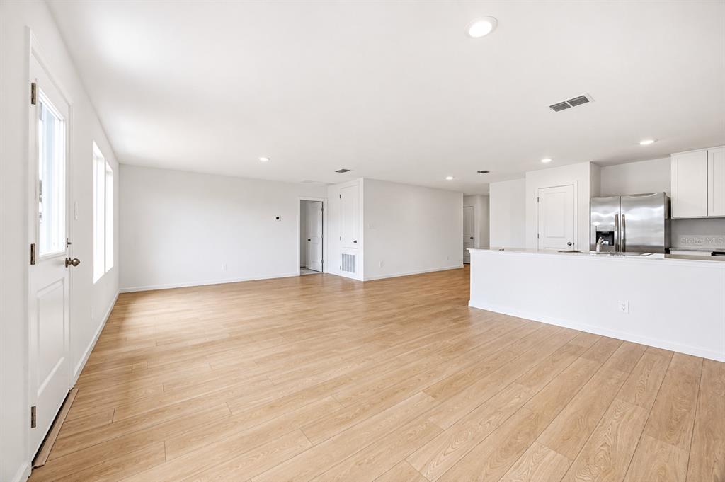 An open-concept living area with light wood-look flooring and a kitchen with white cabinets — 3841 AMERS LOOP, HAINES CITY, FL