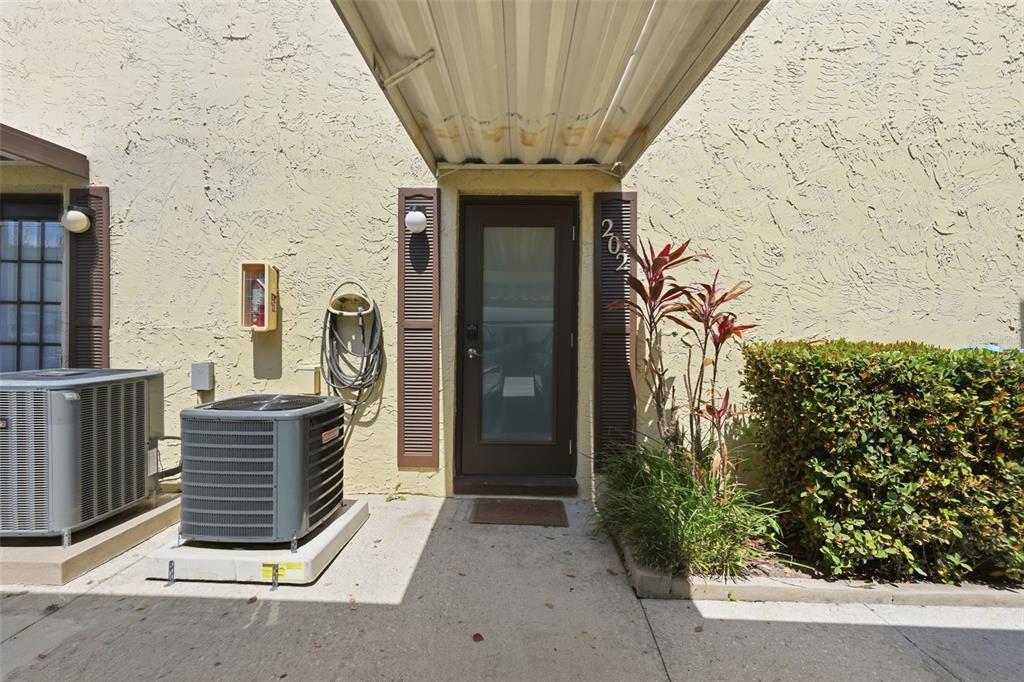 The exterior of a residential unit features a brown door, an air conditioning unit, and landscaping — 501 E BAY DRIVE UNIT 202, LARGO, FL