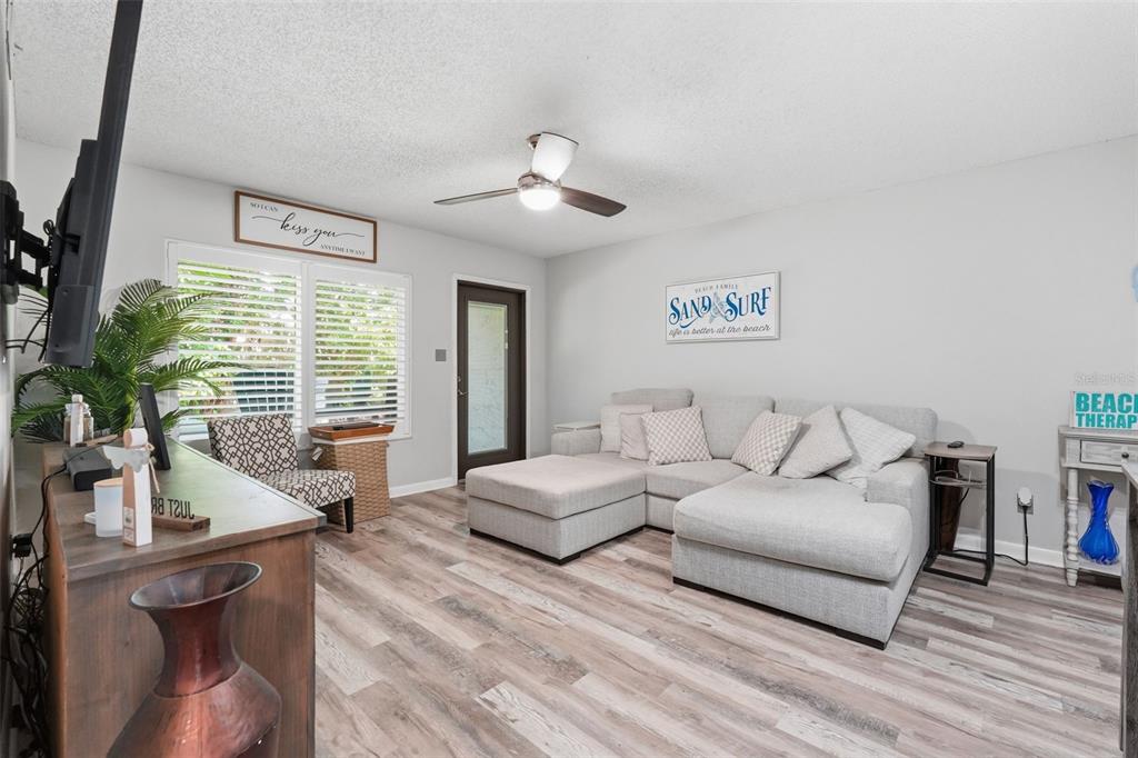 A living room features light wood-look flooring, a gray sectional sofa, and a ceiling fan — 501 E BAY DRIVE UNIT 202, LARGO, FL