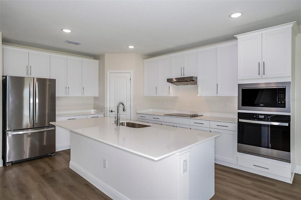 A modern kitchen features white cabinetry, stainless steel appliances, a large island, and wood flooring — 9886 ANNUNCIATION DRIVE, WESLEY CHAPEL, FL