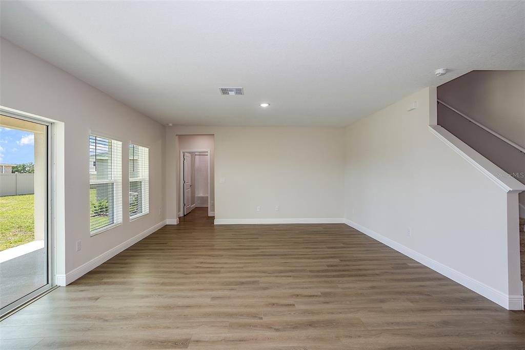 An empty living room features light-colored walls, wood-look flooring, a staircase, and sliding glass doors — 9886 ANNUNCIATION DRIVE, WESLEY CHAPEL, FL