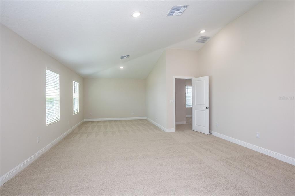 An empty room with beige carpet, light walls, a vaulted ceiling, and an open doorway — 9886 ANNUNCIATION DRIVE, WESLEY CHAPEL, FL