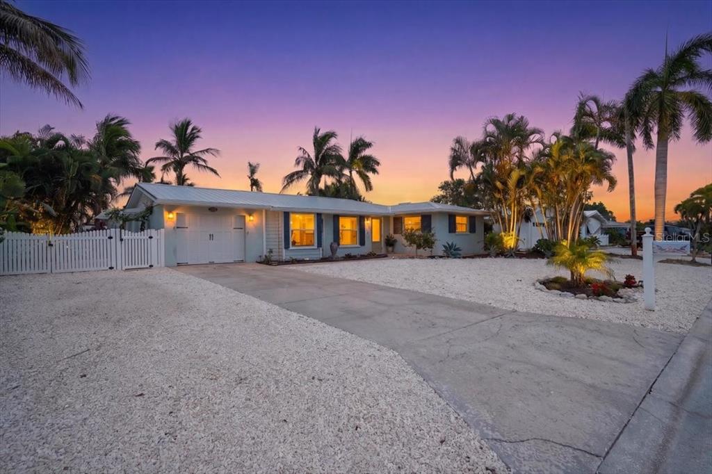 A single-story house with a white garage and gravel yard sits under a sunset sky — 520 69TH STREET, HOLMES BEACH, FL