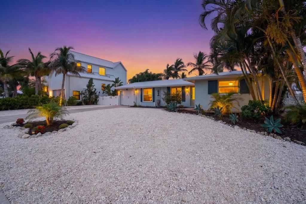 A gravel driveway leads to a one-story house and a taller multi-story building at sunset — 520 69TH STREET, HOLMES BEACH, FL