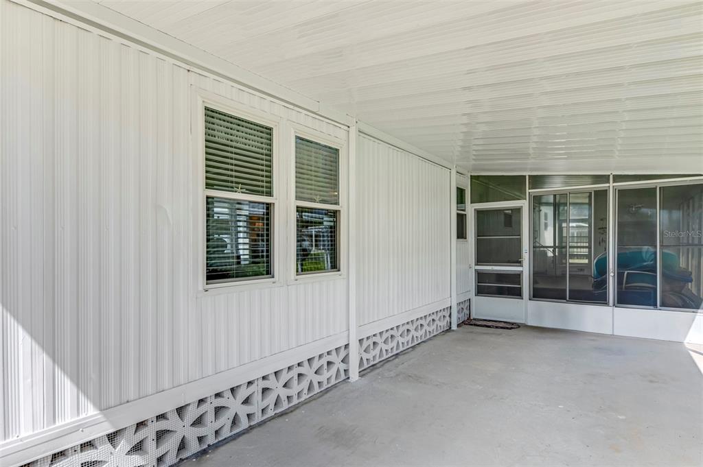 A covered concrete patio features white vertical siding, two windows, and a screened-in entry door — 259 INNER DRIVE E, VENICE, FL