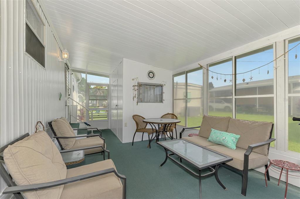 A sunroom features green carpeting, a glass-topped coffee table, a sofa, and two armchairs — 259 INNER DRIVE E, VENICE, FL