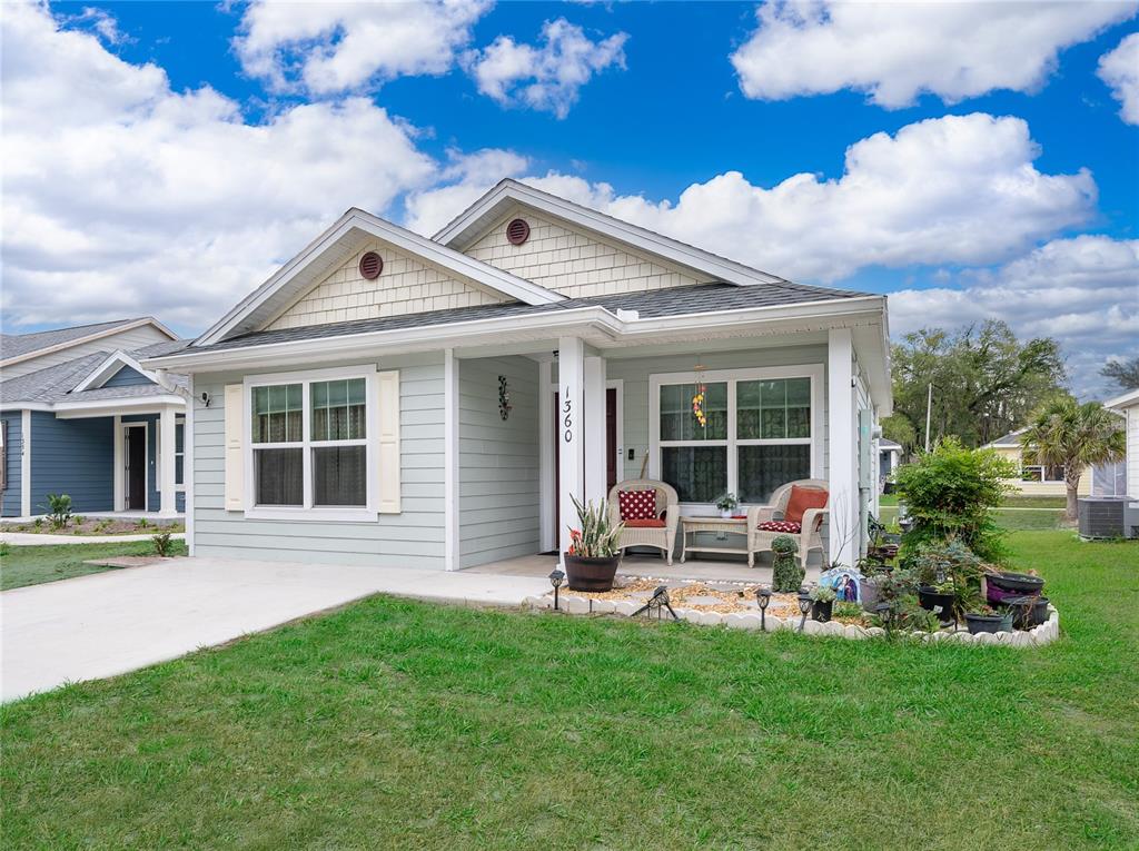 A light green single-story house with a front porch, concrete driveway, and landscaped garden — 1360 COTTAGE CIRCLE, TAVARES, FL