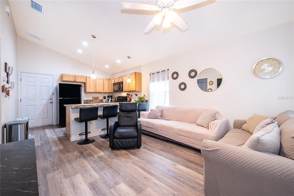 An open-concept living room and kitchen featuring wood-look flooring, a breakfast bar, and two sofas — 1360 COTTAGE CIRCLE, TAVARES, FL