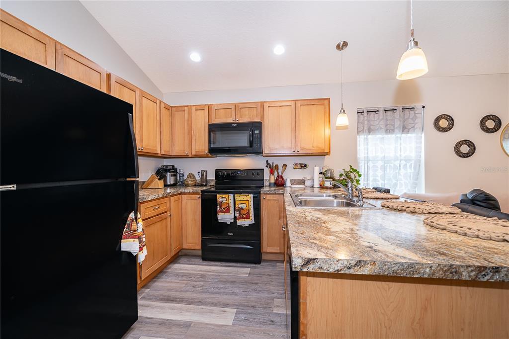 A kitchen features light wood cabinets, black appliances, and a granite-topped island with a sink — 1360 COTTAGE CIRCLE, TAVARES, FL