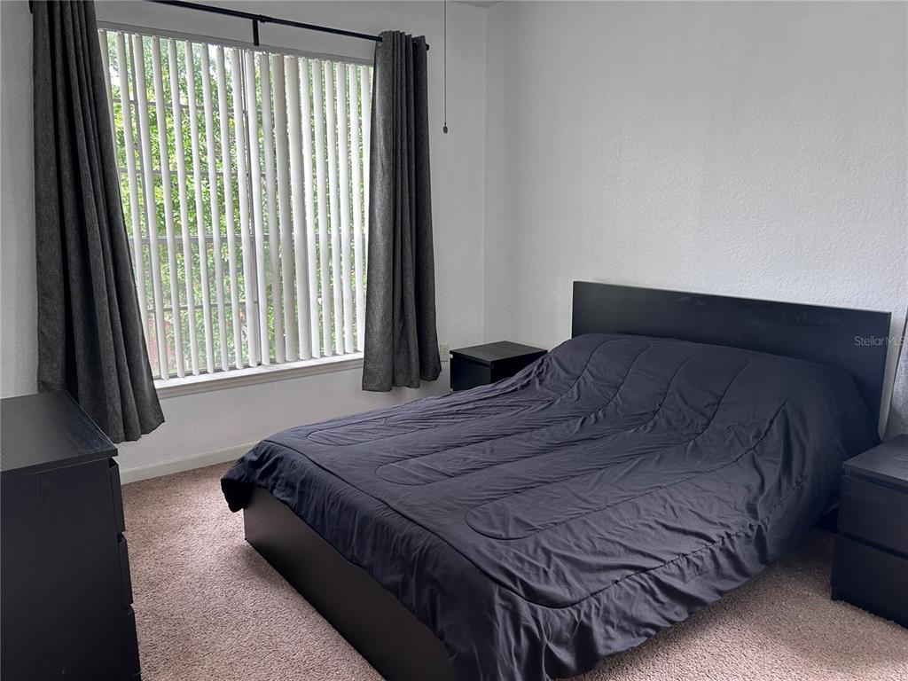 A bedroom features a black bed frame, dark bedding, a nightstand, and vertical window blinds — 13015 PLANTATION PARK CIRCLE UNIT 1031, ORLANDO, FL