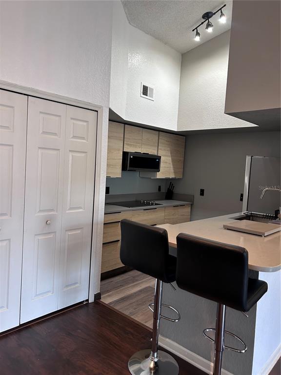 A kitchen features light wood cabinets, a black microwave, and a breakfast bar with stools — 13015 PLANTATION PARK CIRCLE UNIT 1031, ORLANDO, FL