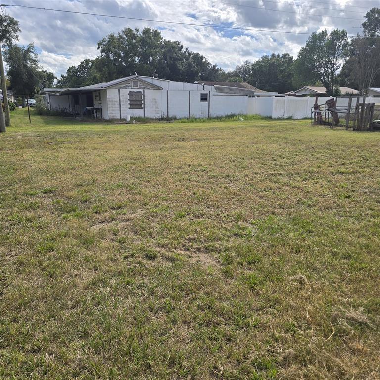 A large, grassy vacant lot sits in front of a white, single-story residential building — 108 E POLK STREET, AUBURNDALE, FL