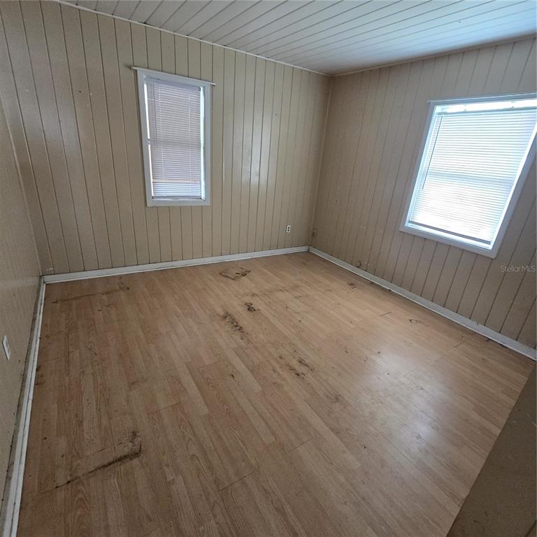 An empty room features light-colored wood-look flooring, beige vertical wall paneling, and two windows — 108 E POLK STREET, AUBURNDALE, FL