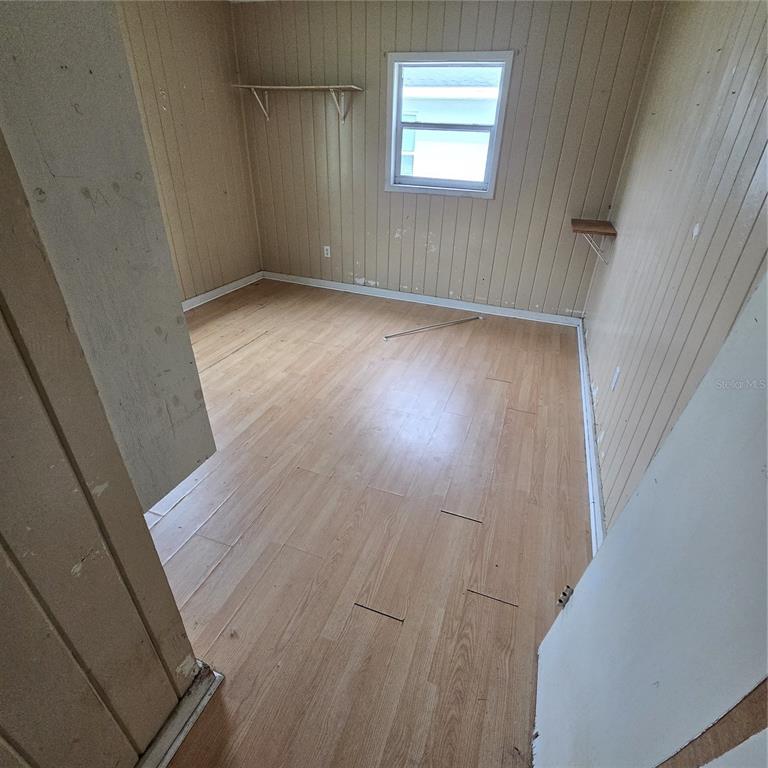 An empty room features light wood-look flooring, vertical wood paneling, and a single window — 108 E POLK STREET, AUBURNDALE, FL