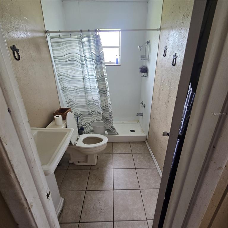 A small bathroom features a pedestal sink, a toilet, and a walk-in shower with tile flooring — 108 E POLK STREET, AUBURNDALE, FL
