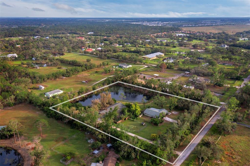 An aerial view shows a residential property with a pond, two houses, and surrounding trees — 5645 CHURCHILL DOWNS ROAD, SARASOTA, FL