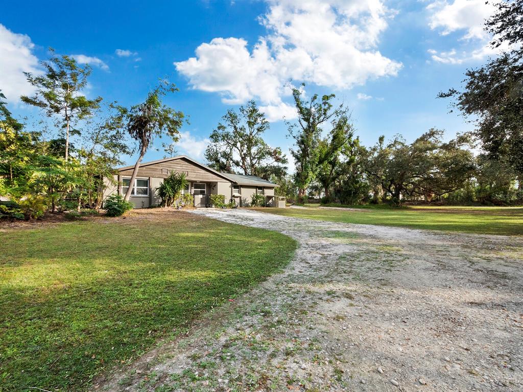 A single-story house with a gravel driveway sits on a large, tree-filled grassy lot — 5645 CHURCHILL DOWNS ROAD, SARASOTA, FL