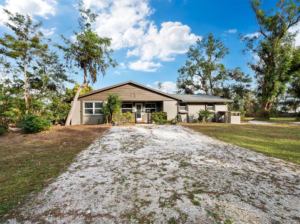 A single-story house with a gravel driveway and surrounding trees under a blue sky — 5645 CHURCHILL DOWNS ROAD, SARASOTA, FL