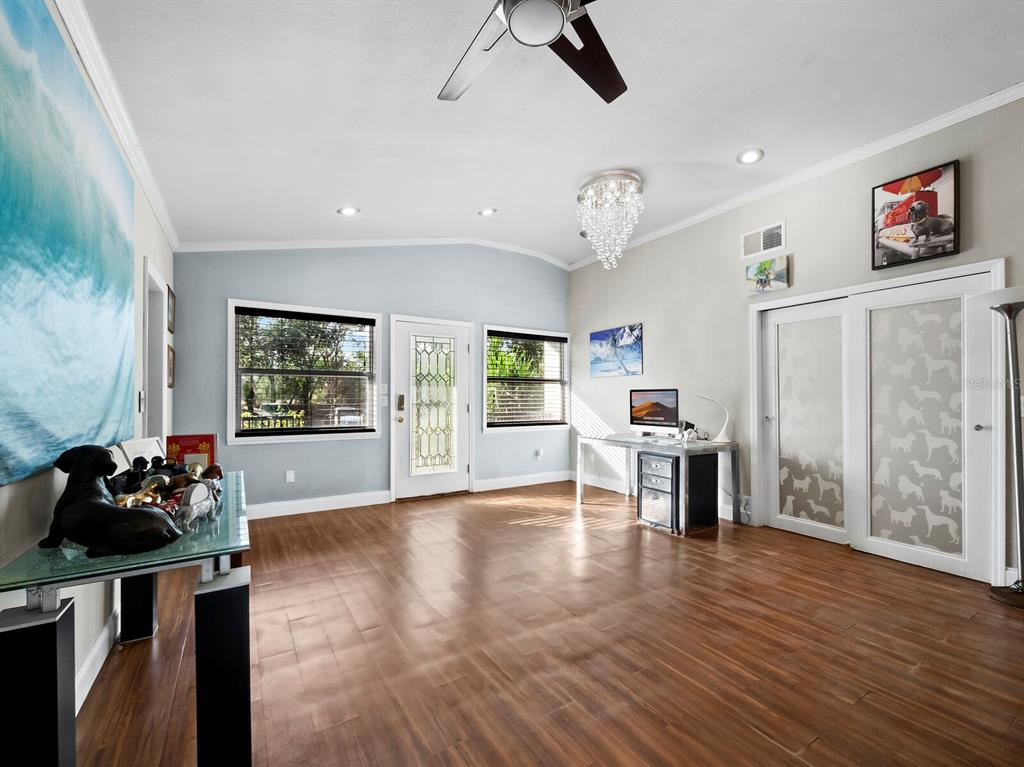 A living room with wood-look flooring, a glass console table, a desk, and sliding doors — 5645 CHURCHILL DOWNS ROAD, SARASOTA, FL