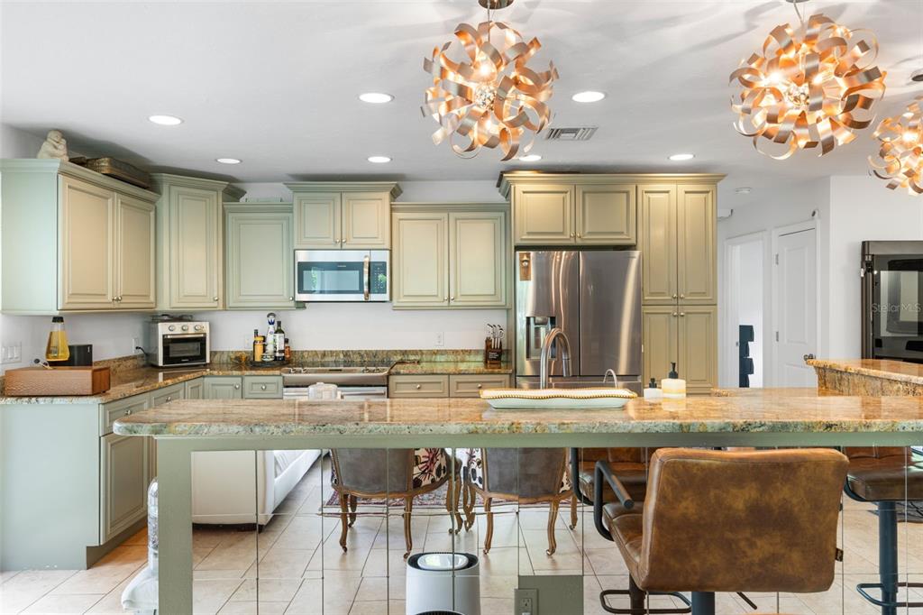 A kitchen features sage green cabinetry, granite countertops, stainless steel appliances, and two decorative pendant lights — 1750 ALTA VISTA STREET, SARASOTA, FL