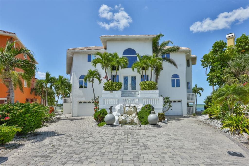 A white multi-story house with a paved driveway, palm trees, and a central rock fountain — 1021 SYMPHONY ISLES BOULEVARD, APOLLO BEACH, FL