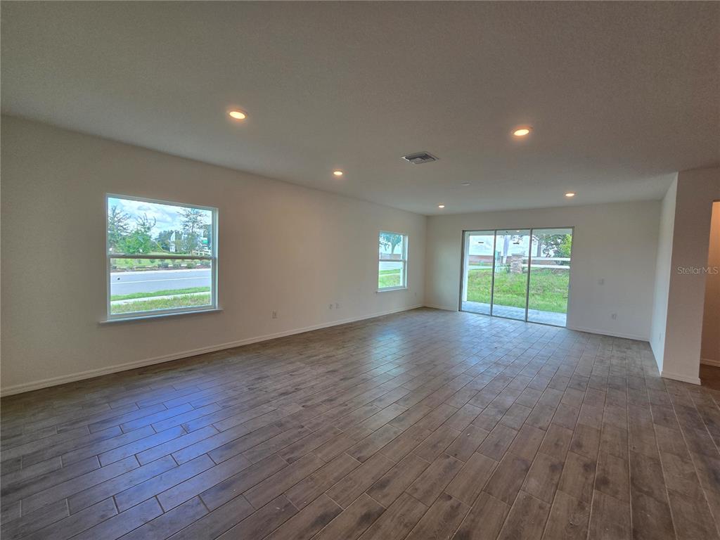 A modern kitchen features white cabinets, a large island with bar stools, and wood-look flooring — 6470 CHORUS DRIVE, MASCOTTE, FL