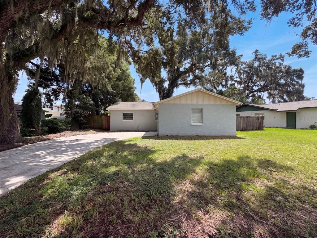 A single-story house with a light-colored exterior, a concrete driveway, and large oak trees — 121 INWOOD CIRCLE, BRANDON, FL