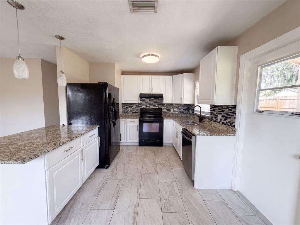 A kitchen with white cabinets, granite countertops, black appliances, and light-colored tile flooring — 121 INWOOD CIRCLE, BRANDON, FL