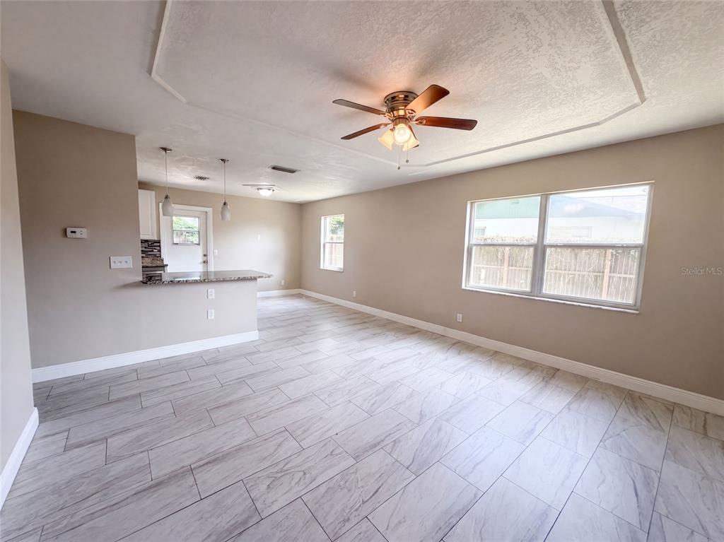 An open-concept living area features light wood-look tile flooring, a ceiling fan, and a kitchen — 121 INWOOD CIRCLE, BRANDON, FL