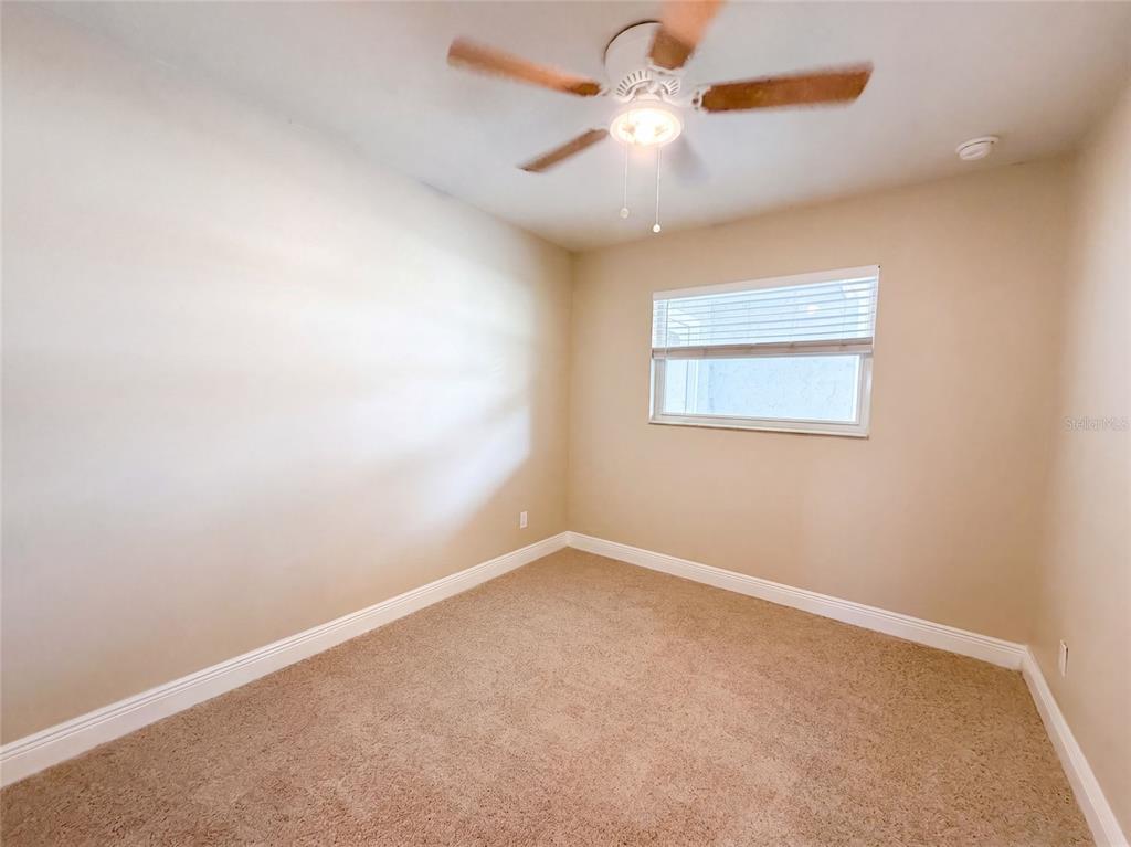 An empty bedroom features beige walls, tan carpeting, a ceiling fan, and a single window — 121 INWOOD CIRCLE, BRANDON, FL