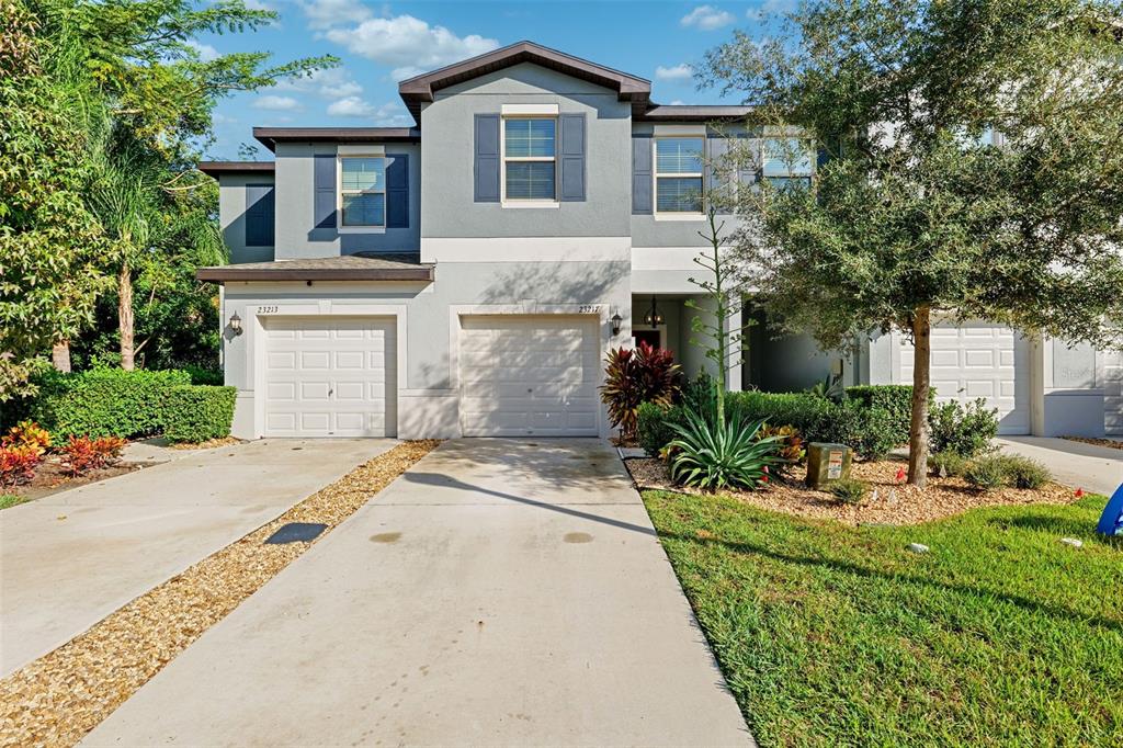 A two-story duplex with gray stucco siding, two garage doors, and a concrete driveway — 23217 WILLOW GLEN WAY, LUTZ, FL