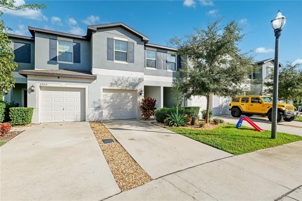 A two-story townhouse exterior features two garage doors, a concrete driveway, and a yellow Jeep — 23217 WILLOW GLEN WAY, LUTZ, FL