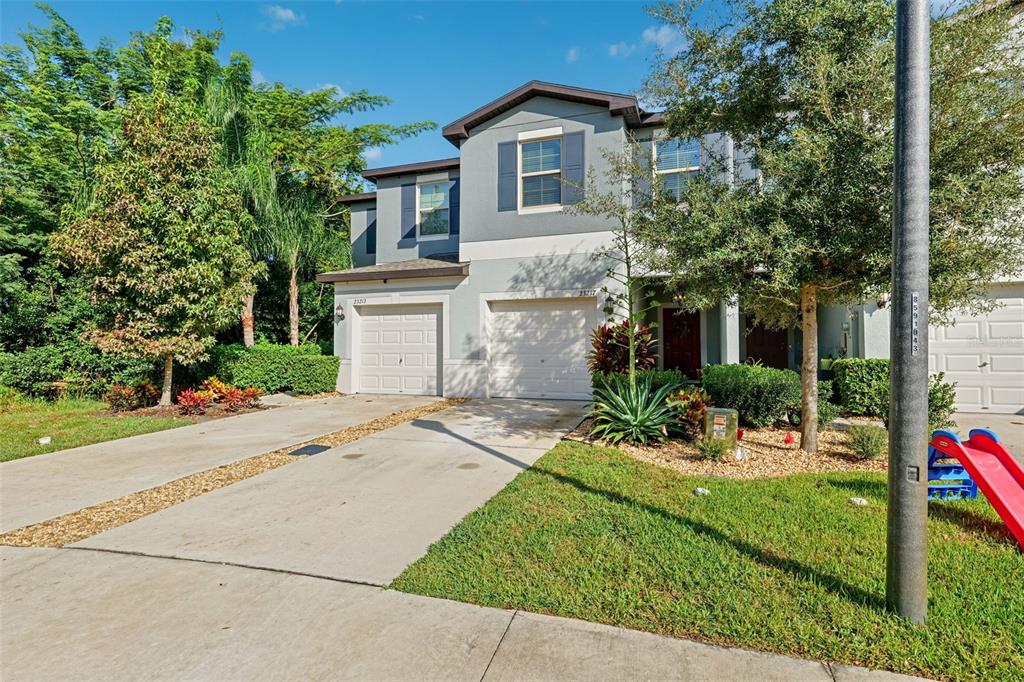 A two-story townhouse with a gray facade, two garage doors, and a front lawn — 23217 WILLOW GLEN WAY, LUTZ, FL